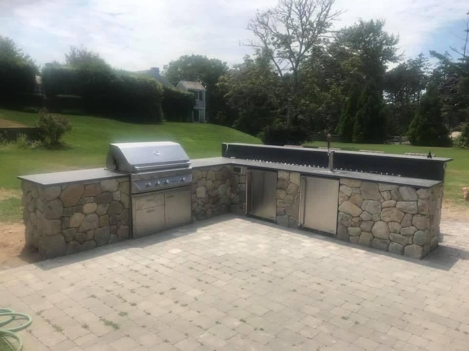 Outdoor kitchen with stone countertops and stainless steel grill in a spacious yard.