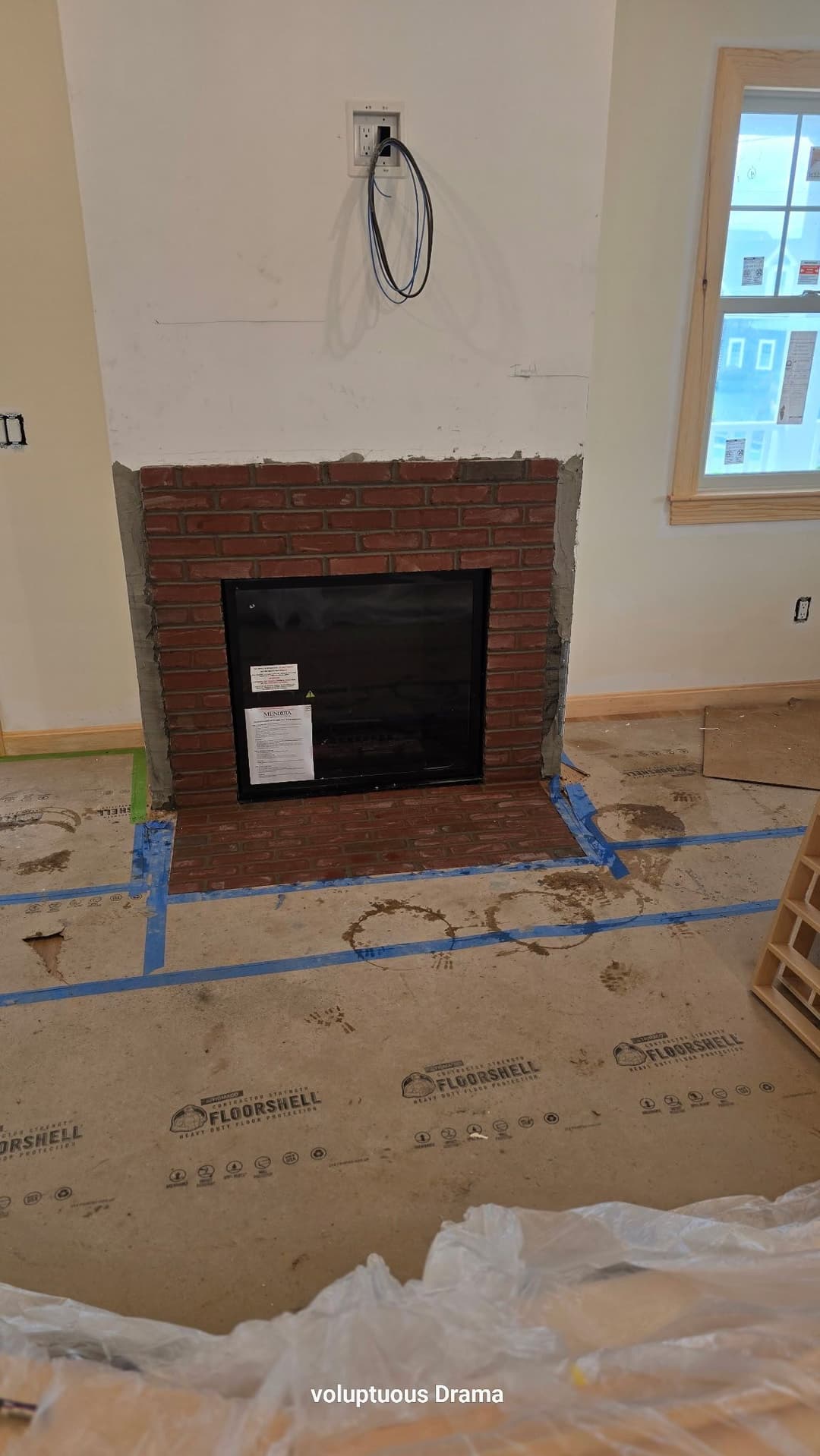 Modern brick fireplace under construction in a renovated home with floor markings.