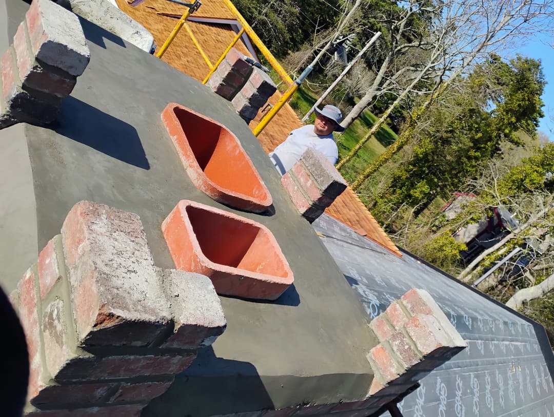 Construction worker installing bricks and clay pots on a roof with trees in the background.