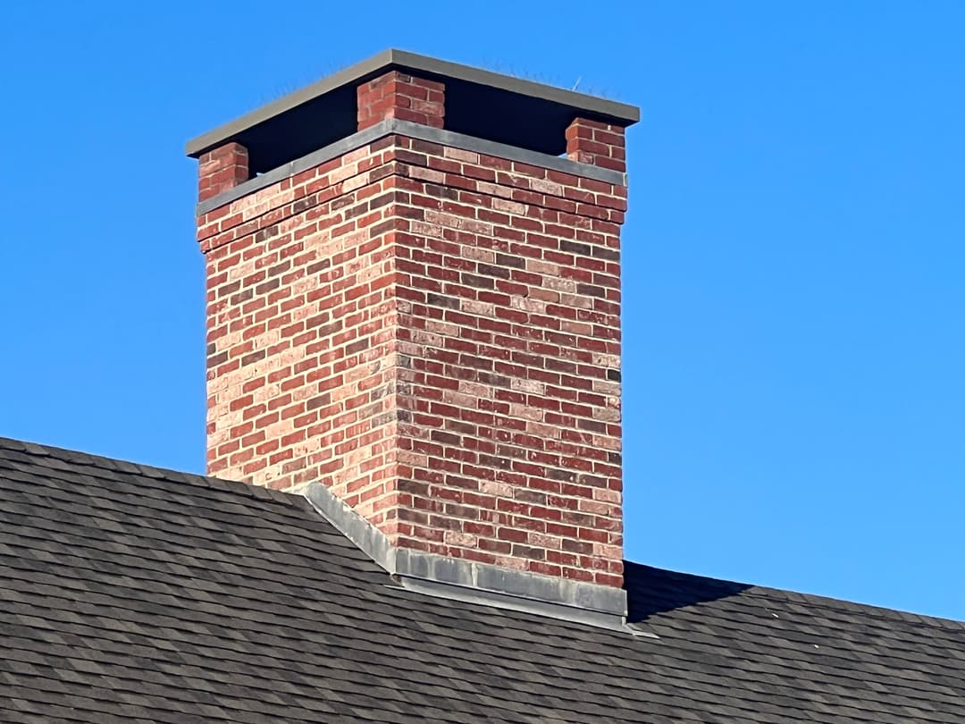 Brick chimney on a sloped roof against a clear blue sky, showcasing architectural detail.