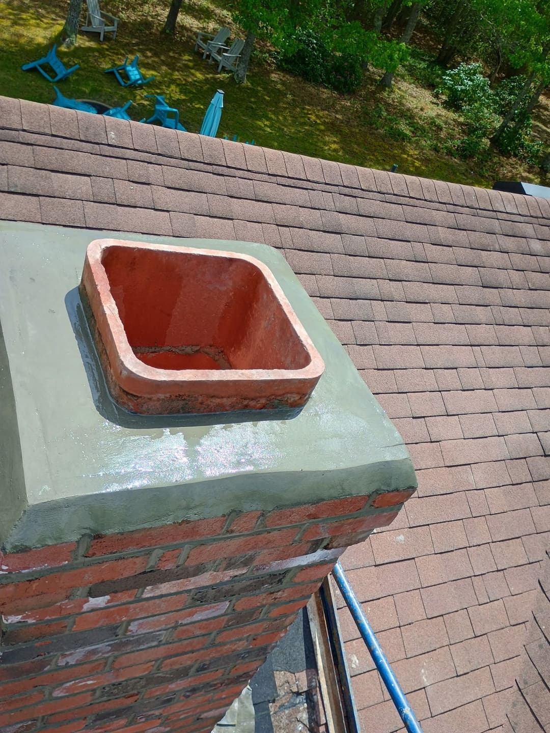 Chimney top view showing a red clay flue and newly coated gray chimney cap on a roof.