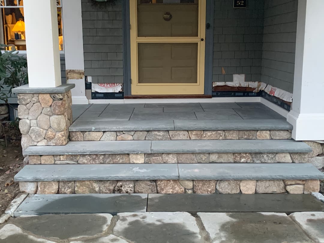 Stone steps with gray slate landing leading to a front door, surrounded by porch columns.