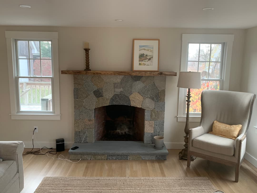 Cozy living room featuring a stone fireplace, armchair, and natural light from windows.