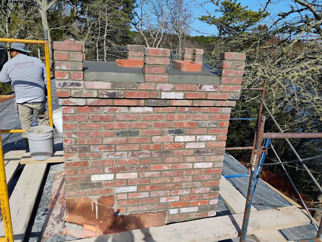 Chimney repair with brick structure and copper cap atop a rooftop under construction.