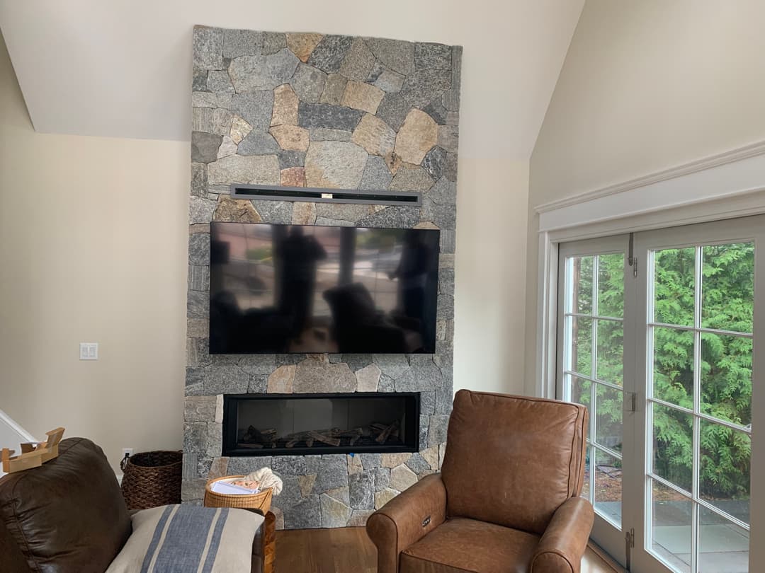 Modern living room with a stone fireplace, wall-mounted TV, and a comfortable brown armchair.