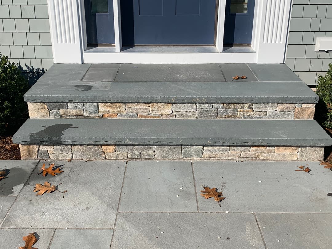 Stone steps leading to a modern home entrance with autumn leaves on the ground.