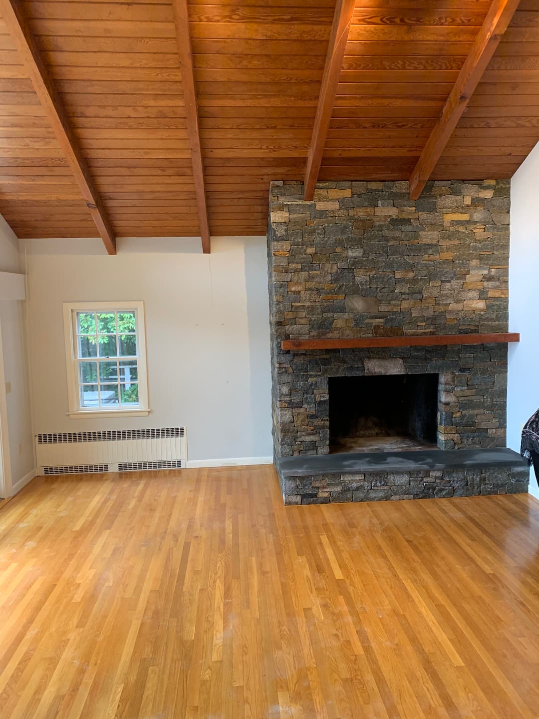 Spacious living room with wooden beams, stone fireplace, and hardwood flooring.