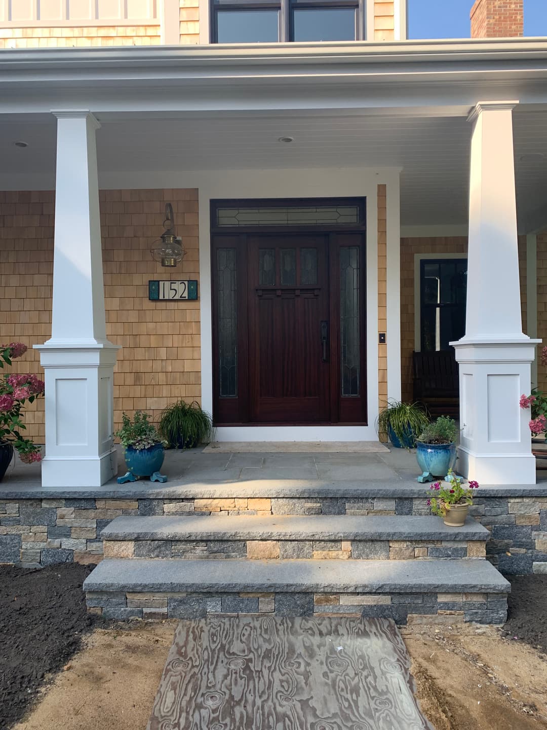 Front entrance of a house featuring wooden door, stone steps, and landscaped details.