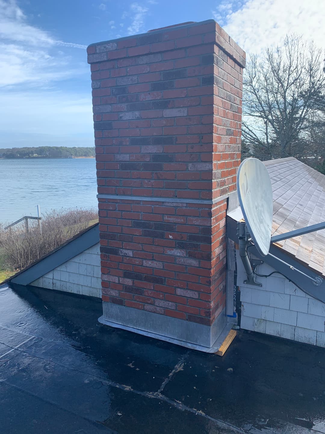 Brick chimney on a rooftop overlooking a lake, with a satellite dish nearby.