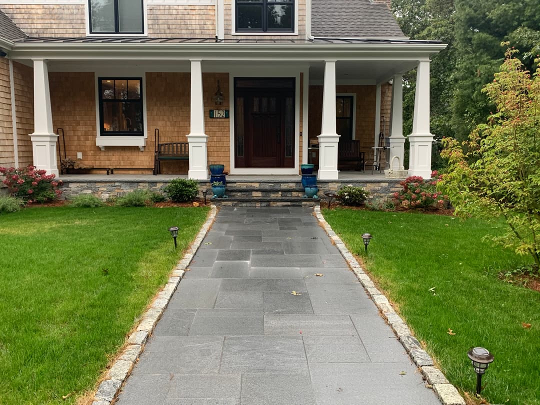 Welcoming porch with stone walkway, lush green lawn, and decorative plants. Ideal home entrance.