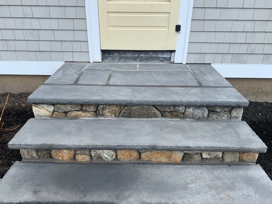 Gray stone and concrete steps leading to a yellow door on a house.