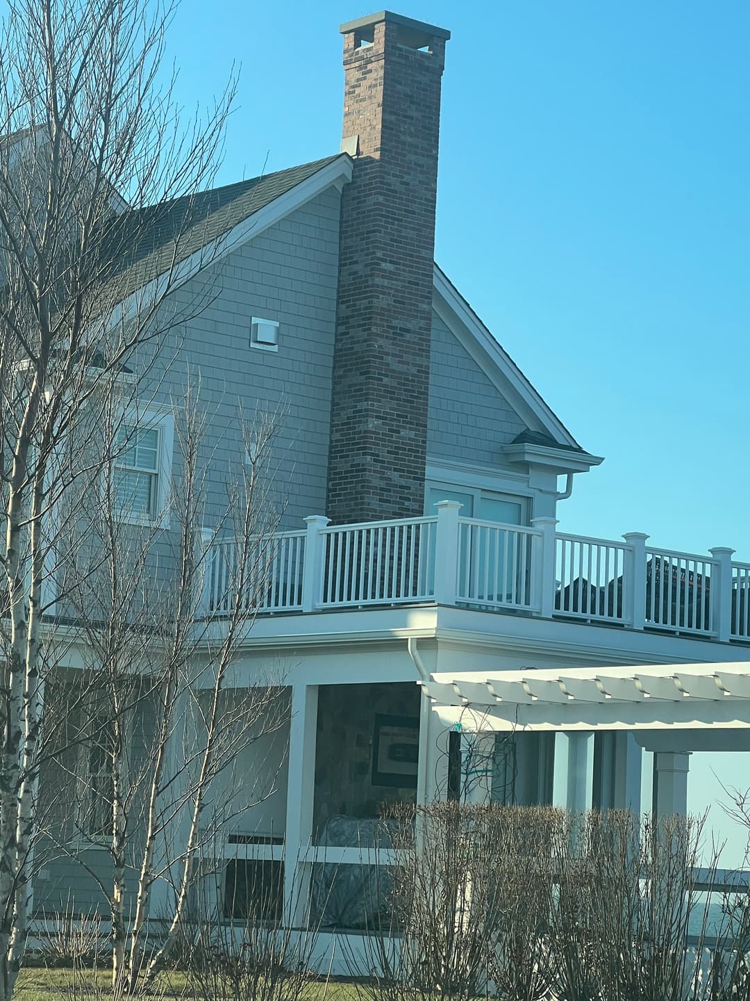 Cozy two-story house with a brick chimney and a white railing porch under a clear blue sky.