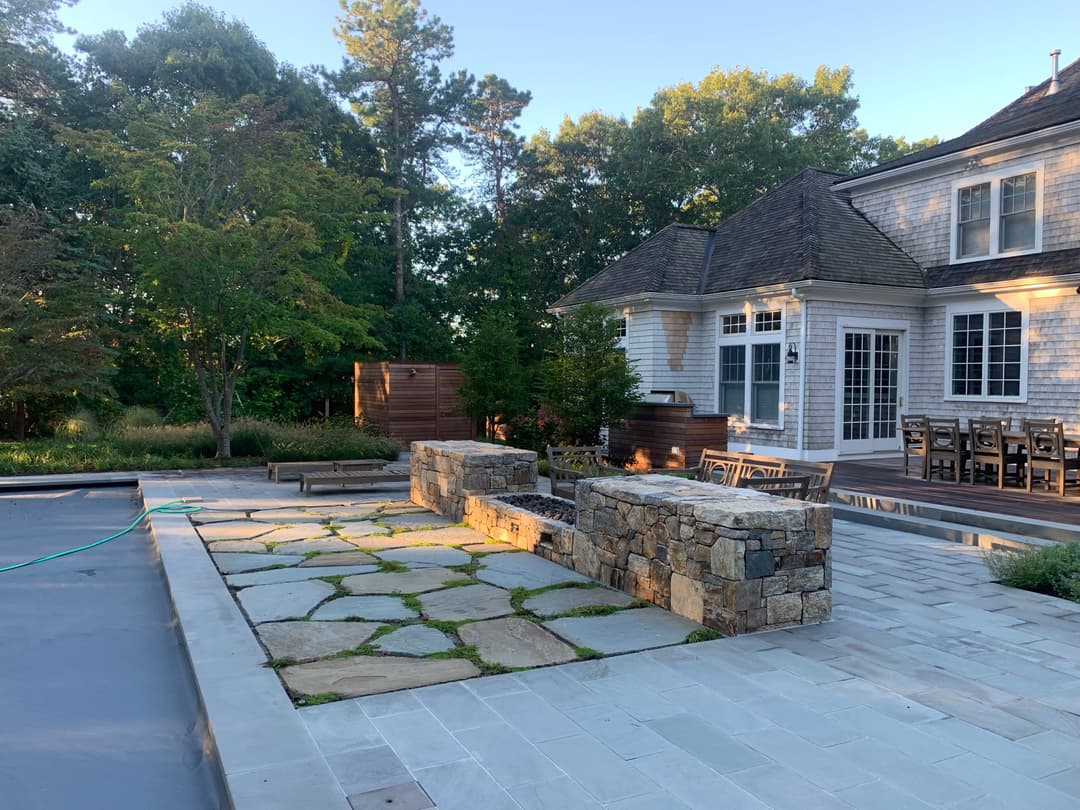 Outdoor patio with stone seating, landscaped garden, and a modern house in a serene setting.