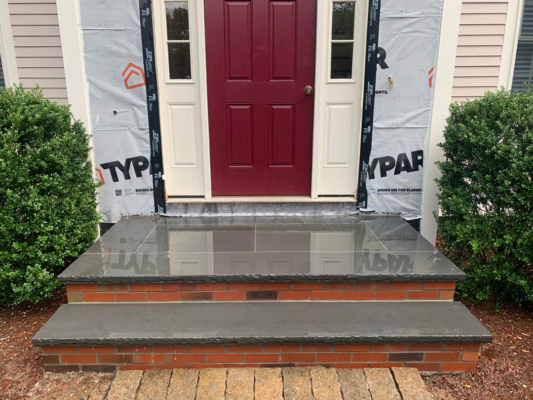 Newly installed slate steps leading up to a maroon front door with brick and greenery.
