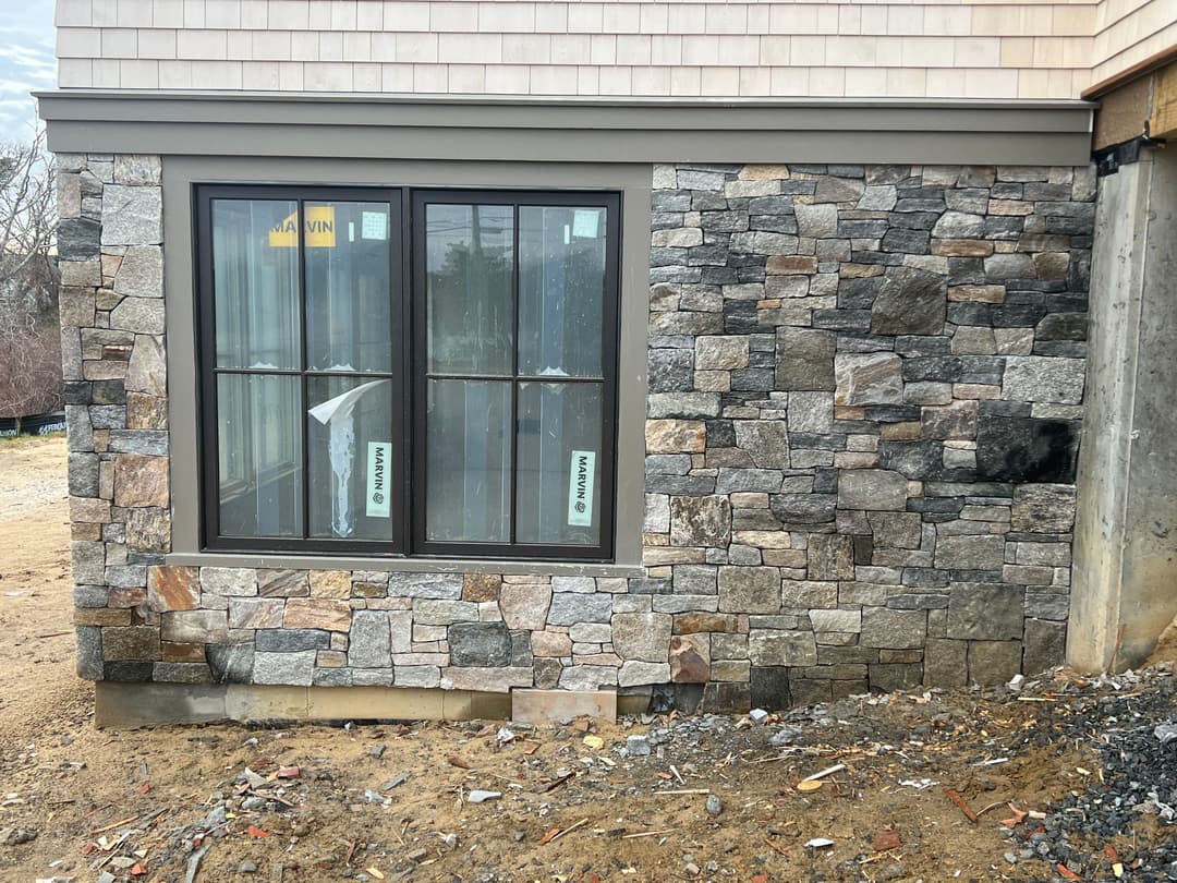 Stone exterior wall with large windows under construction at a residential building.