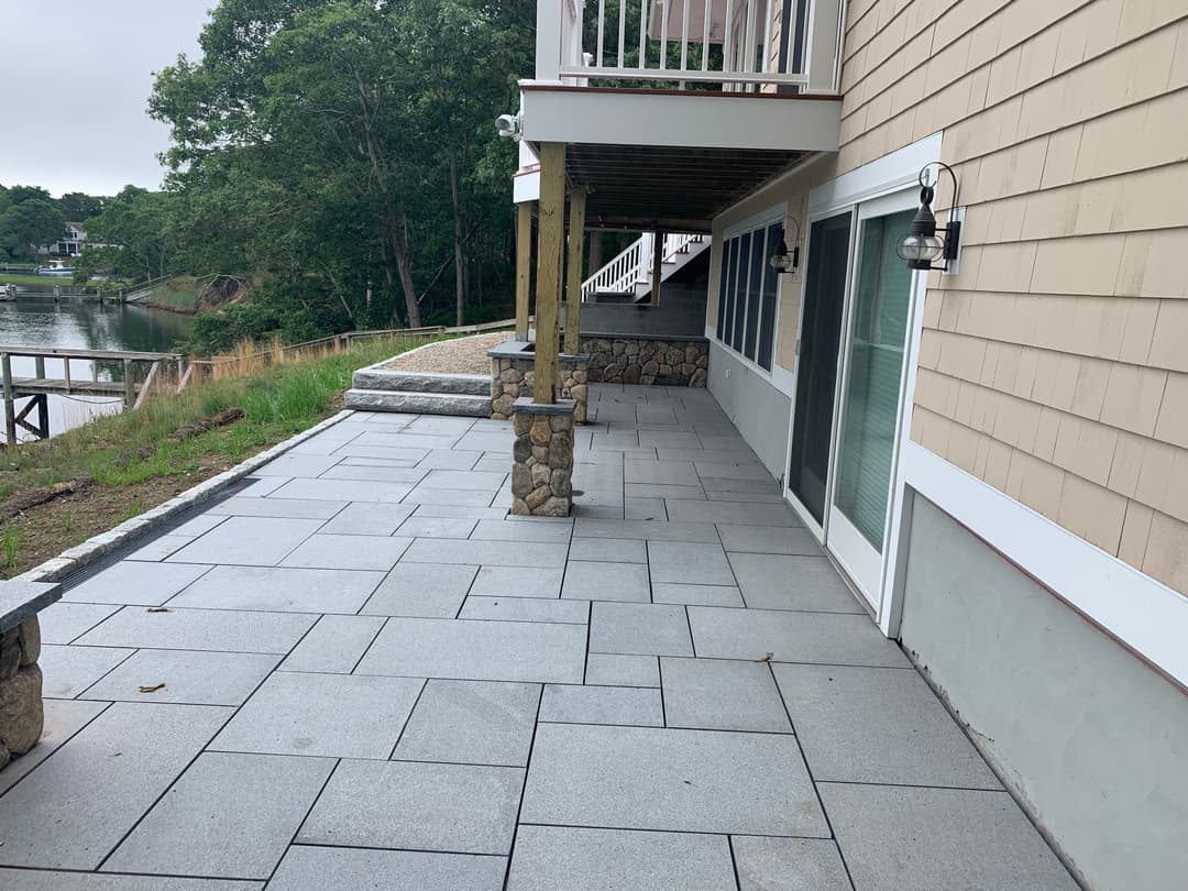 Patio area with gray stone pavers, outdoor lamps, and a view of a serene waterfront.