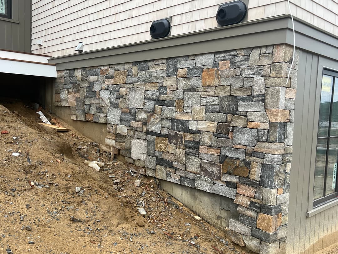 Exterior view of a building showcasing a stone veneer wall and a sloped landscape.