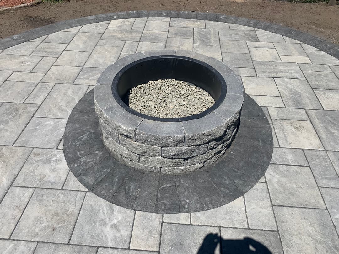 Stone fire pit surrounded by circular paved patio, featuring gray stone pavers and gravel.