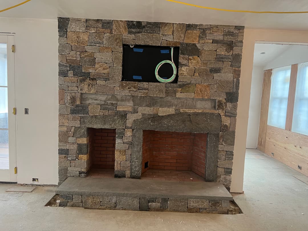 Stone fireplace with dual openings, under construction, in a bright interior space.