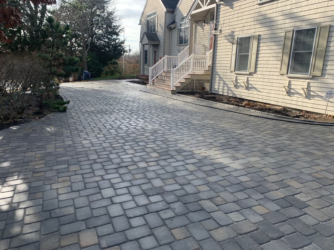Paved driveway with concrete pavers leading to a house and landscaped garden.