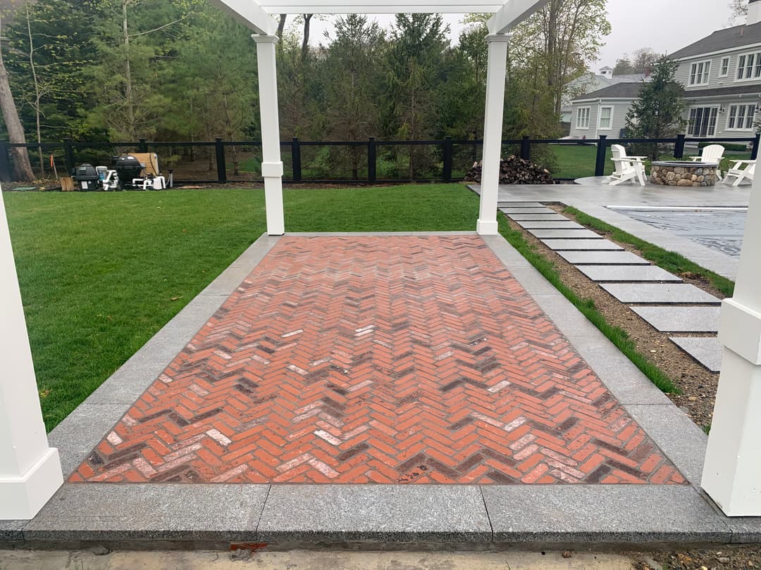 Herringbone brick patio with stone borders in a landscaped backyard setting.