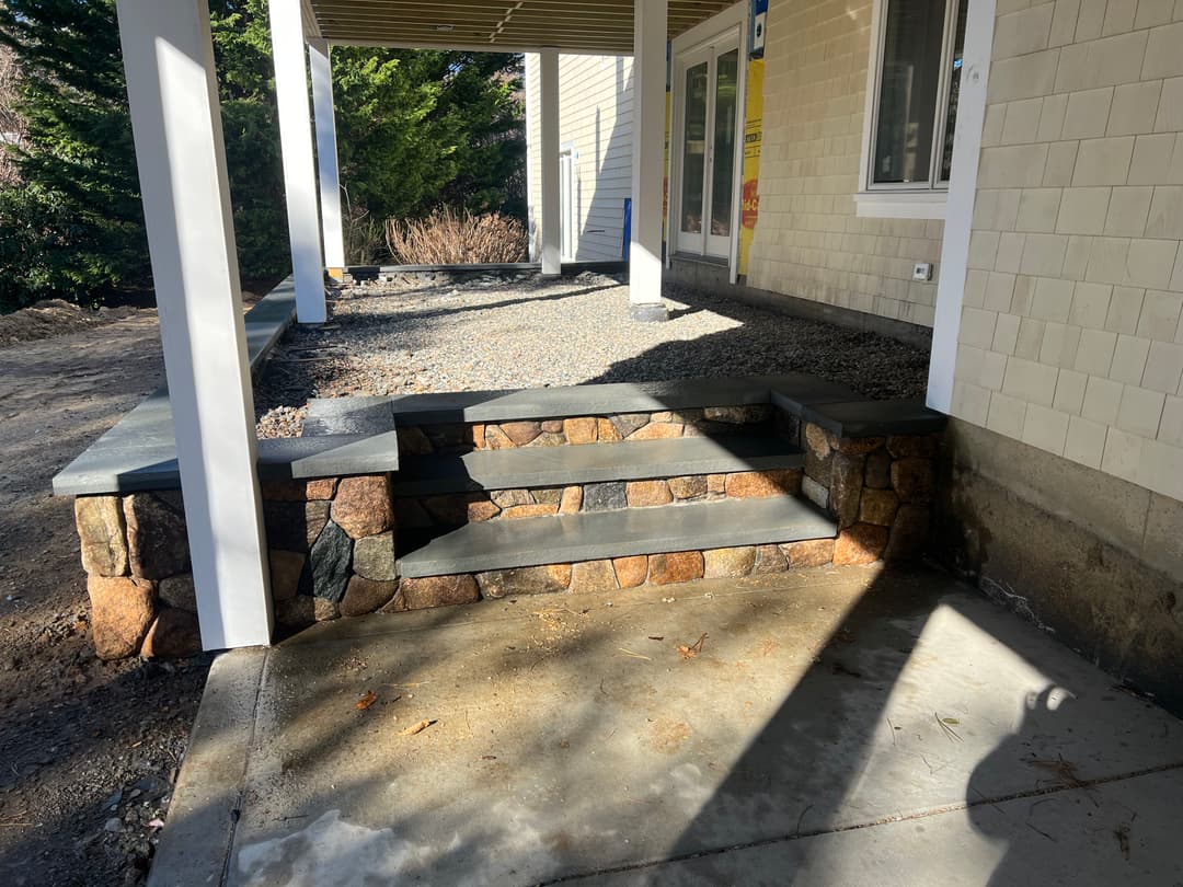 Stone steps leading to a house entrance with a covered porch and landscaped surroundings.