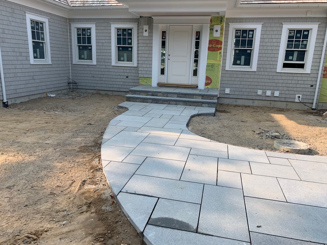 Newly installed stone pathway leading to a home entrance with gray siding and unfinished landscaping.