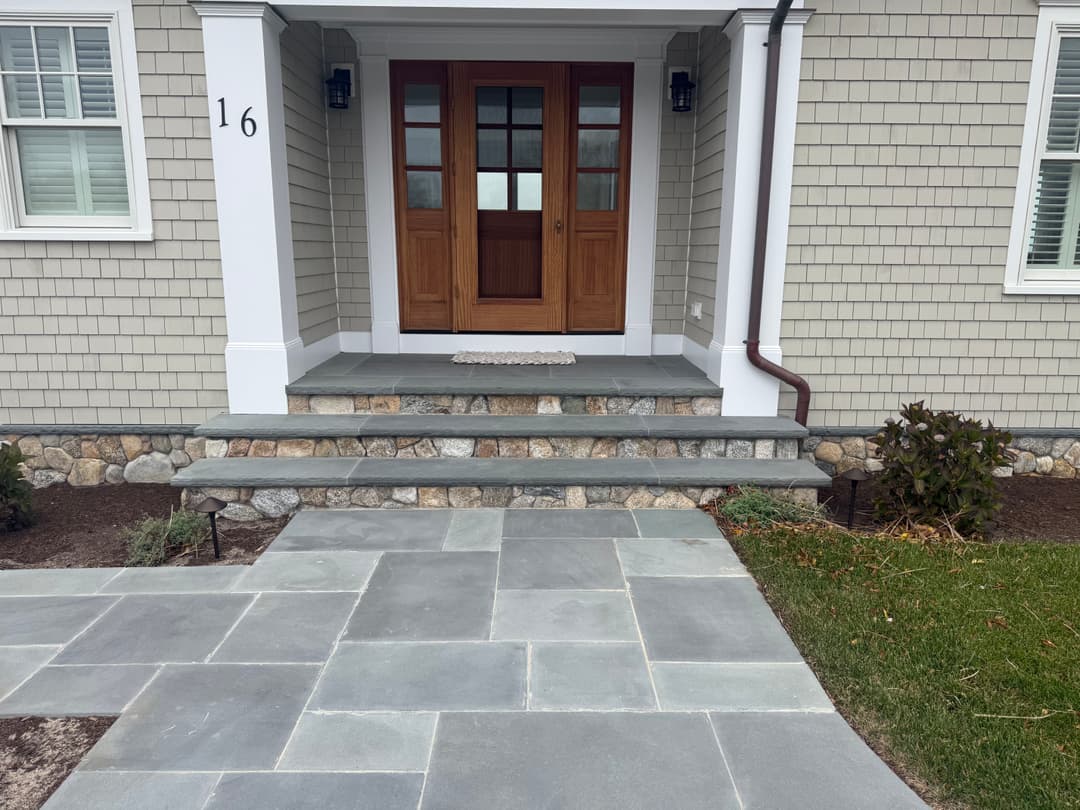 Modern entrance with slate steps, wooden doors, and stone landscaping at a residential home.