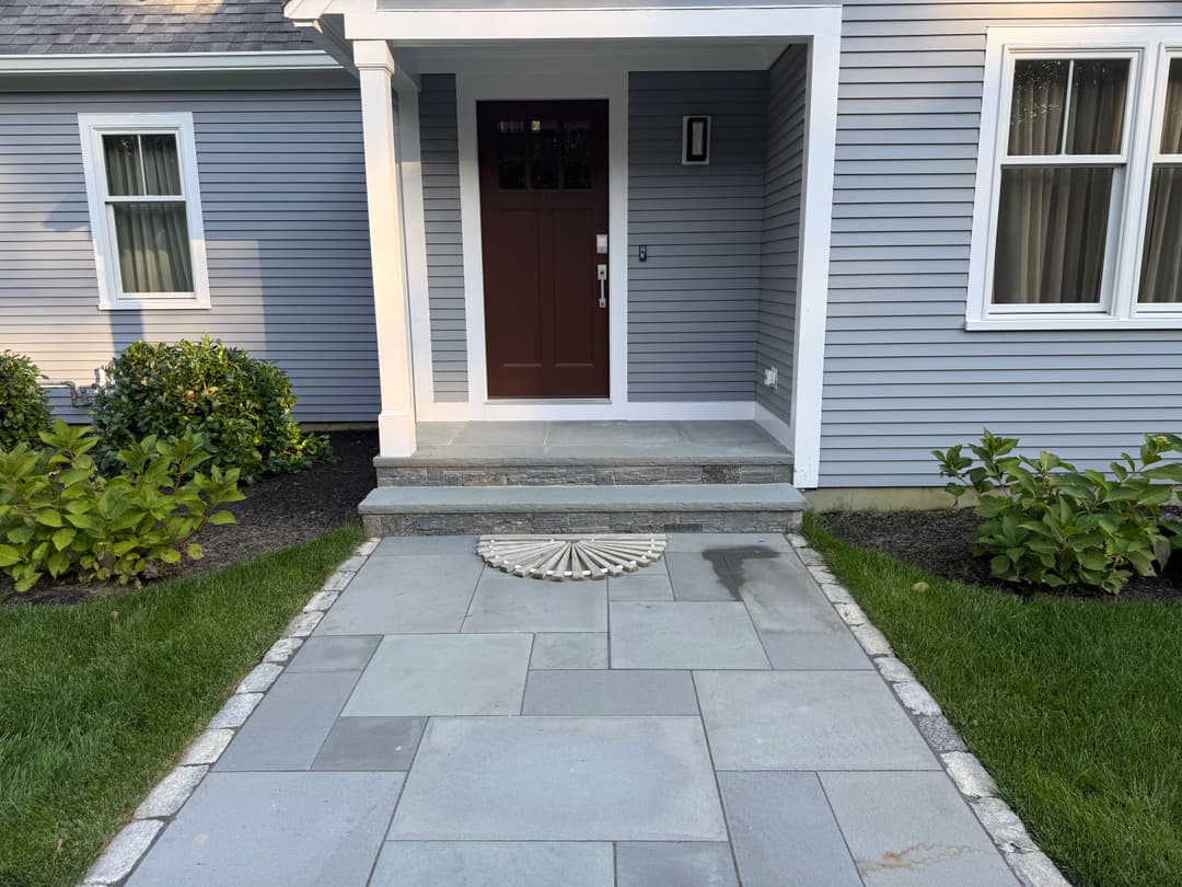 Front entrance of a modern home with a brown door, stone steps, and sleek pathway.
