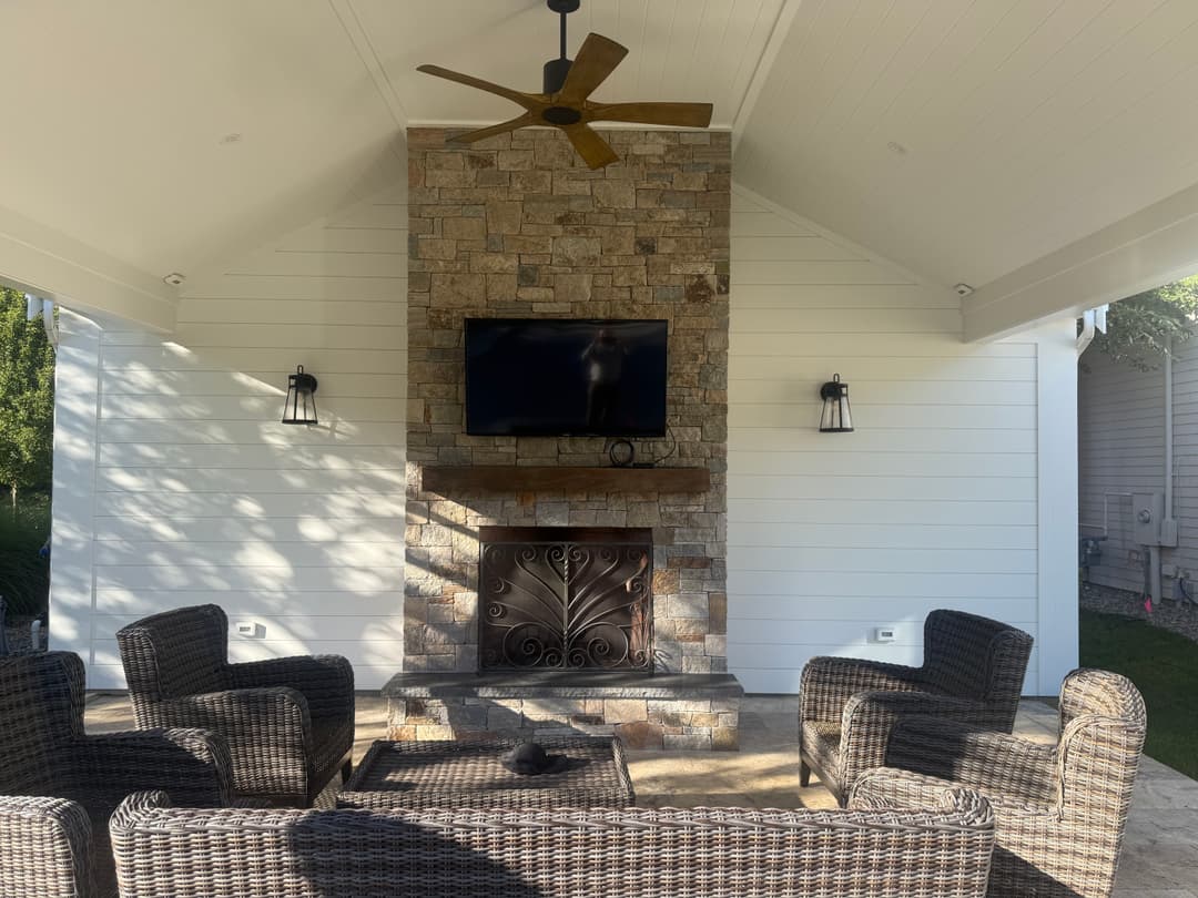 Cozy outdoor patio with stone fireplace, TV, and wicker seating under a covered shelter.