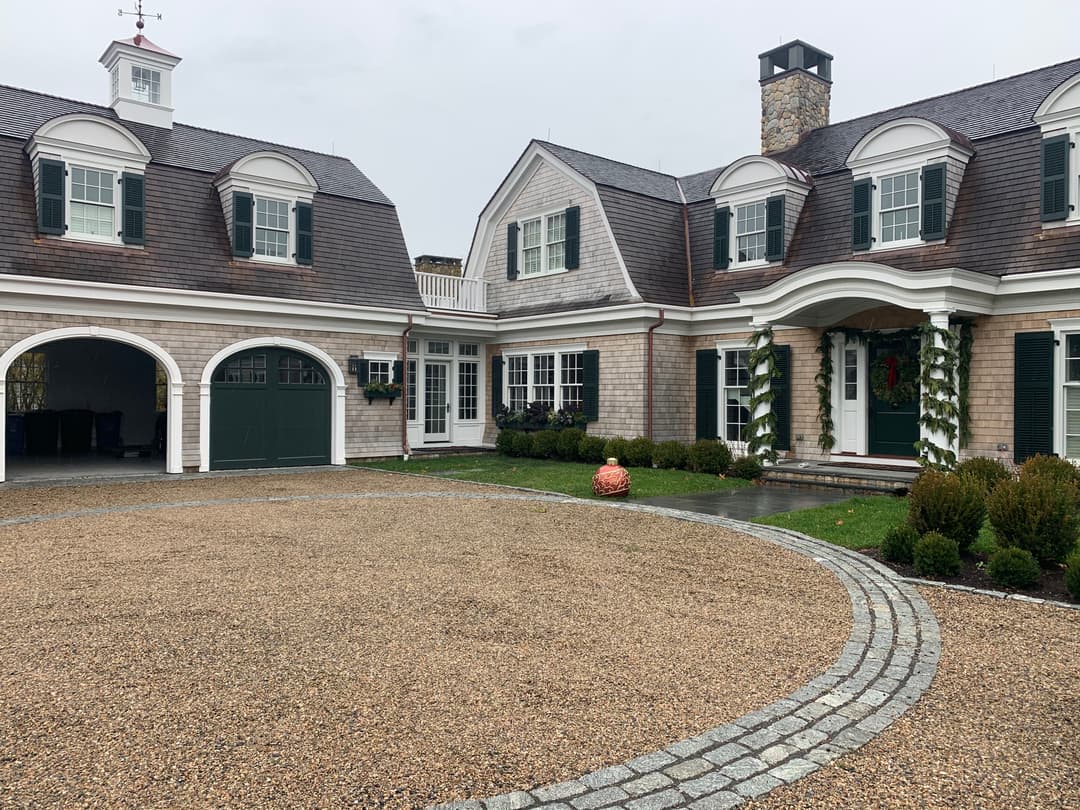 Elegant modern house with stone accents, green shutters, and landscaped gravel driveway.