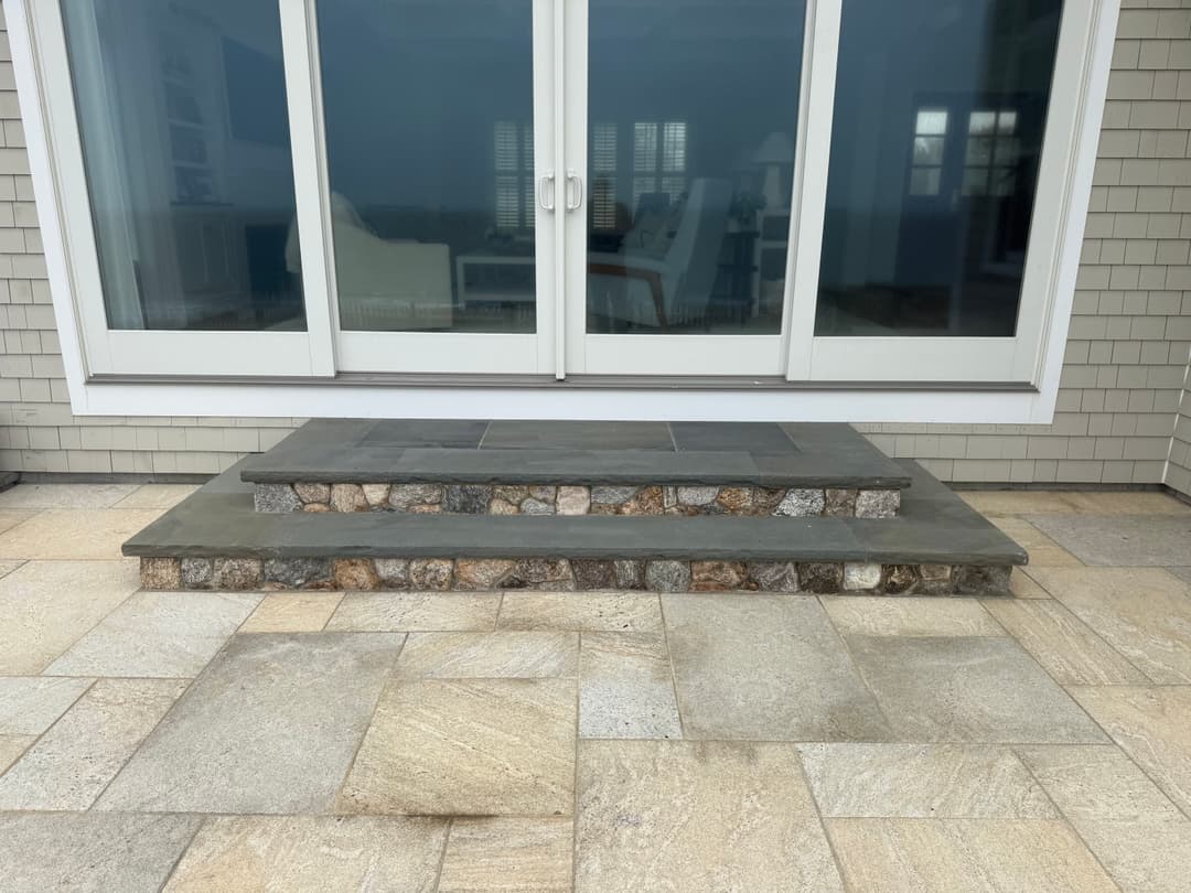 Slate steps with stone accents leading to a large glass door and patio area.