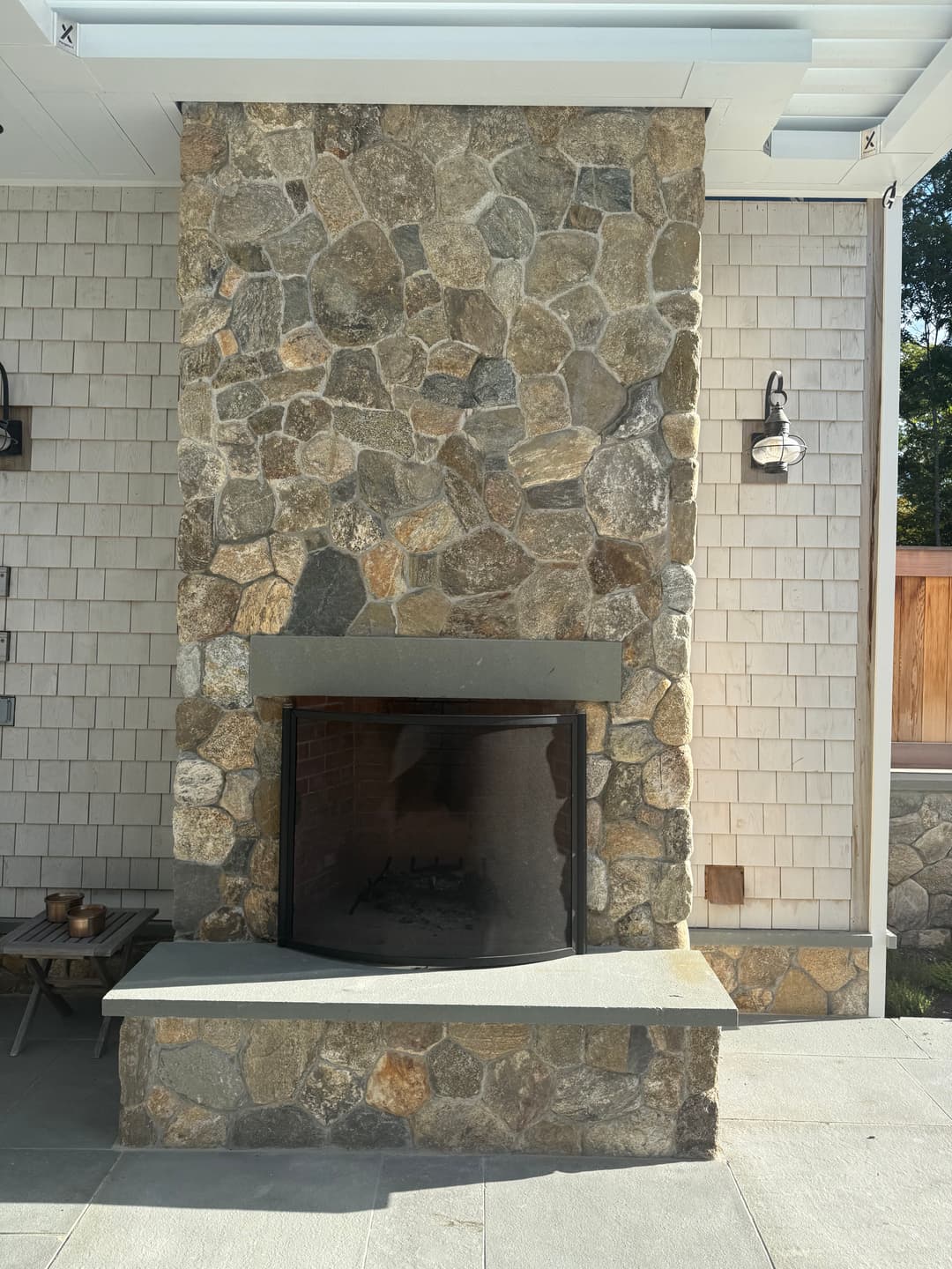 Stone outdoor fireplace with a sleek design, surrounded by light-colored siding and patio area.