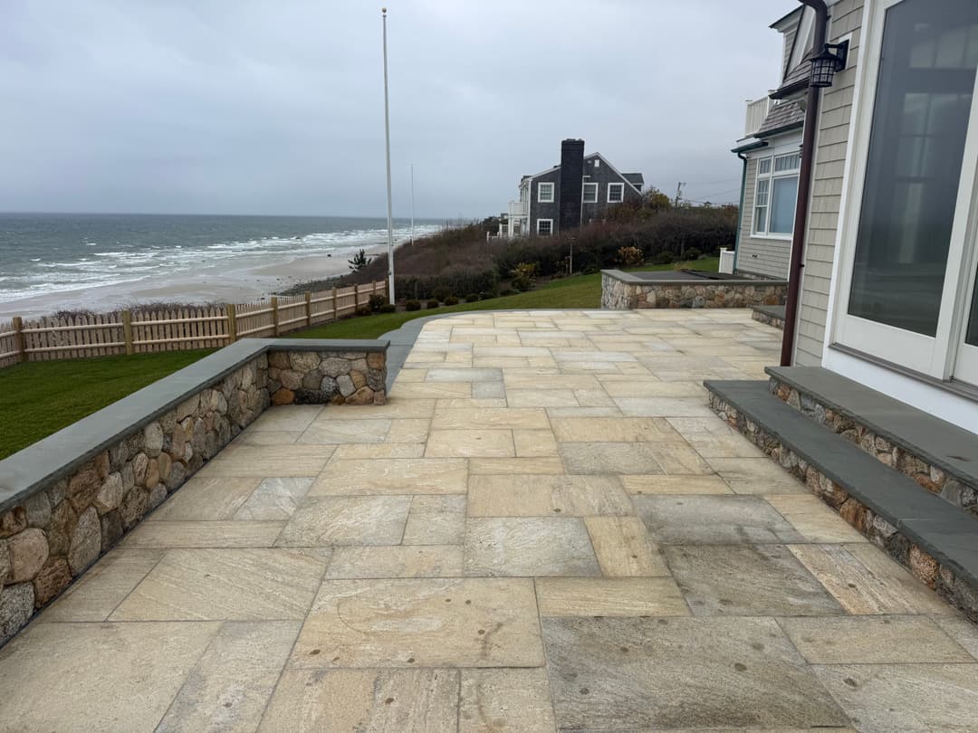 Coastal patio with stone paving overlooking the ocean and beach houses in the background.