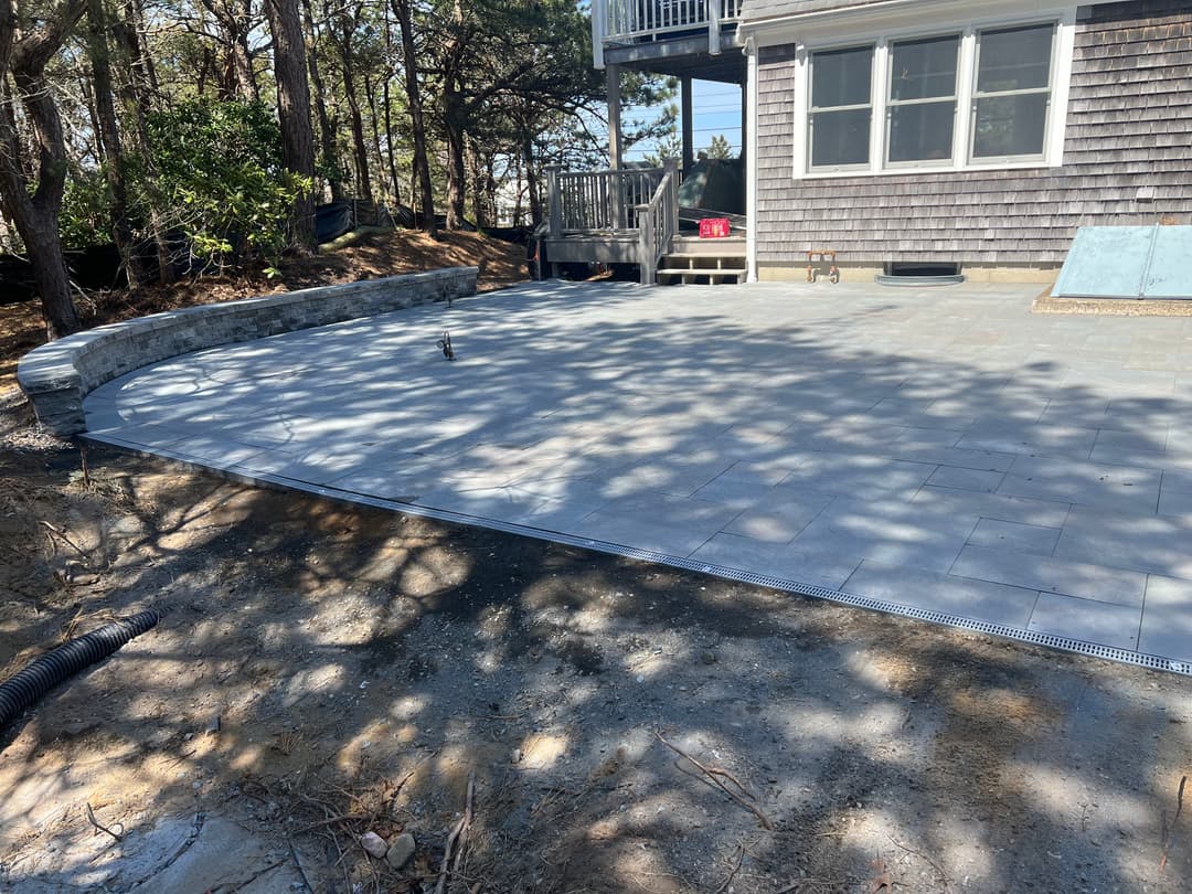 Newly paved outdoor patio with stone tiles, surrounded by trees and a house exterior.
