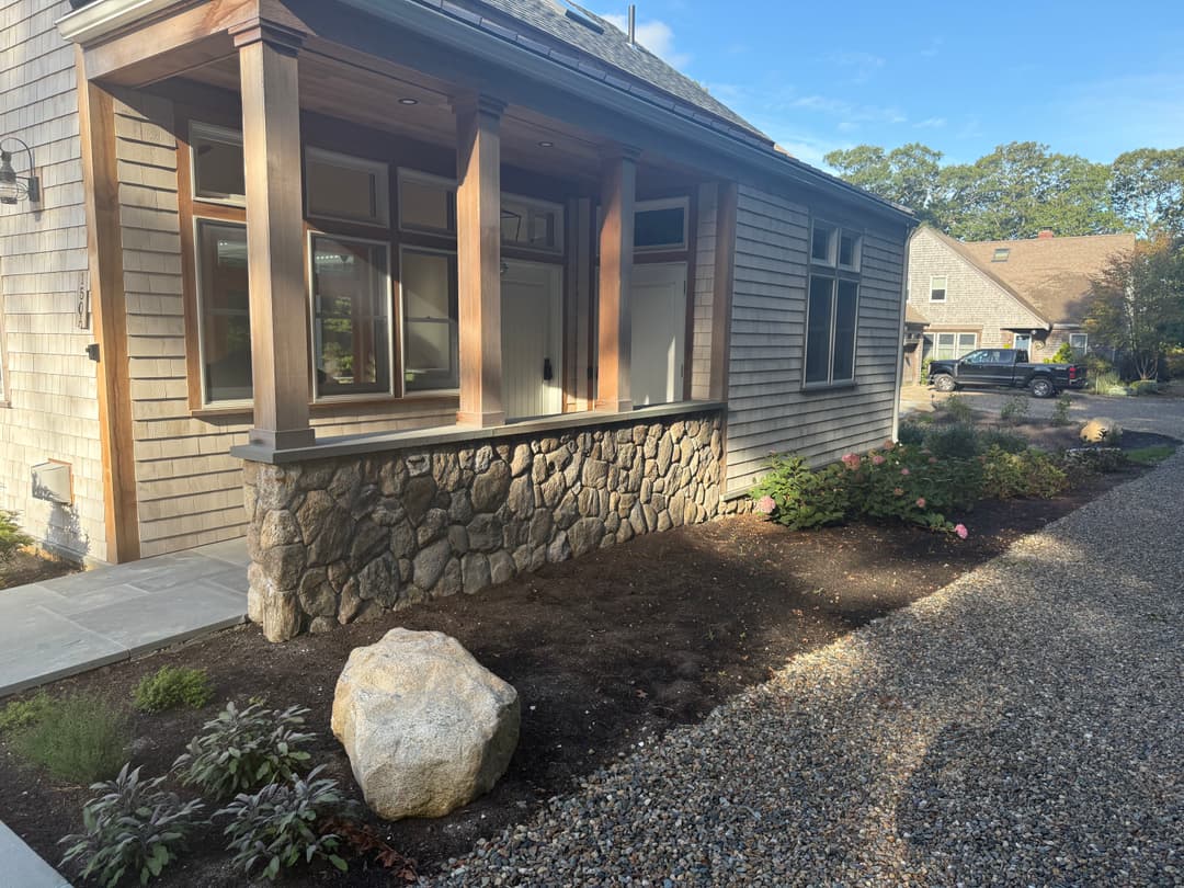 Charming home exterior with stone accents, landscaped garden, and gravel driveway.