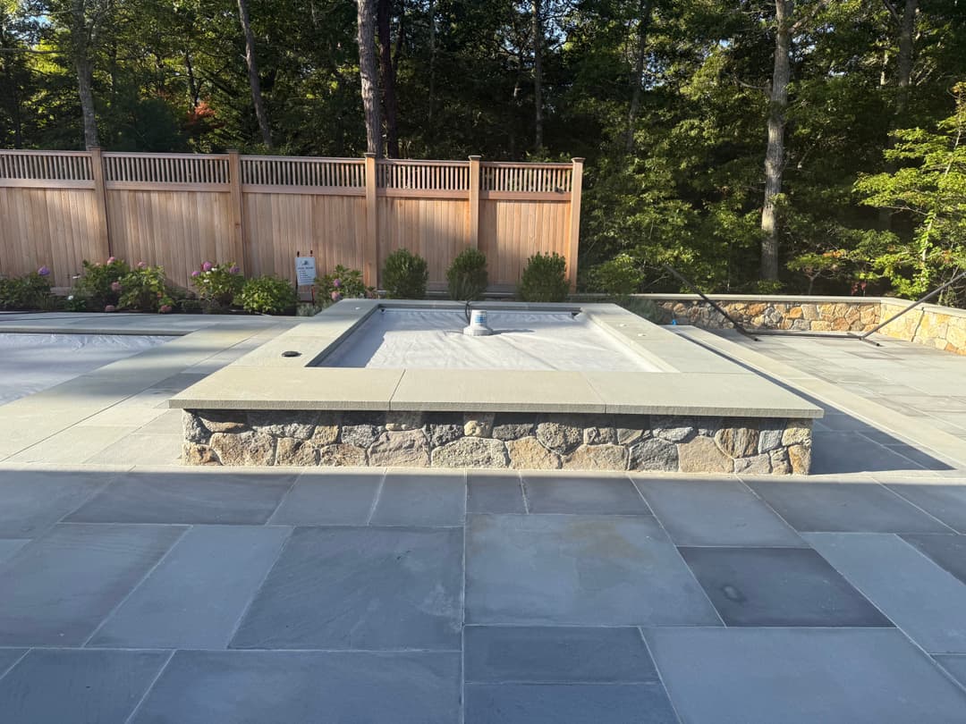 Modern pool with stone surround and wooden fencing in a landscaped backyard setting.