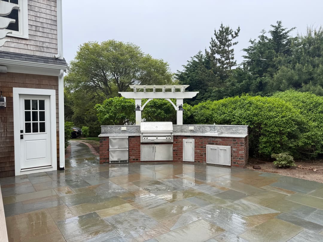 Modern outdoor kitchen with stainless steel appliances and clean brick accents on a rainy day.