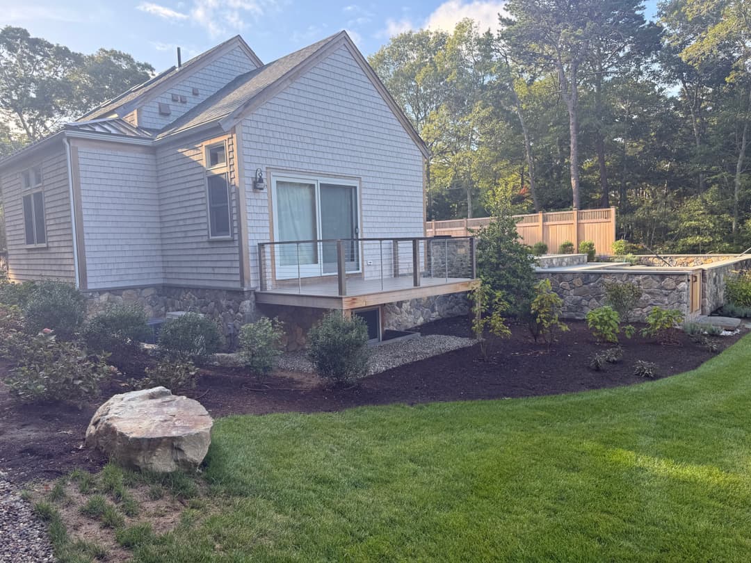 Modern house exterior with deck, landscaped garden, and stone details, under clear skies.