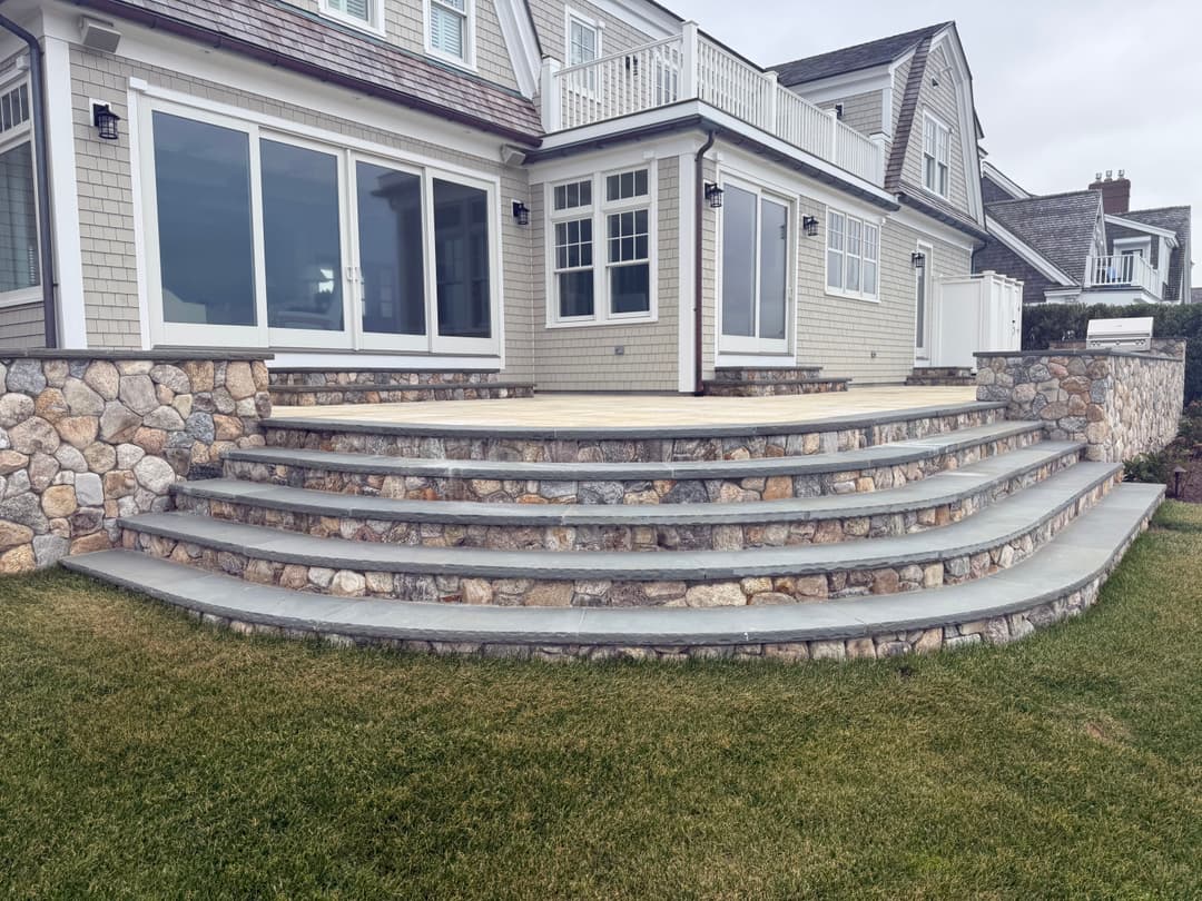 Stone staircase leading to a modern coastal house with large windows and a grassy lawn.