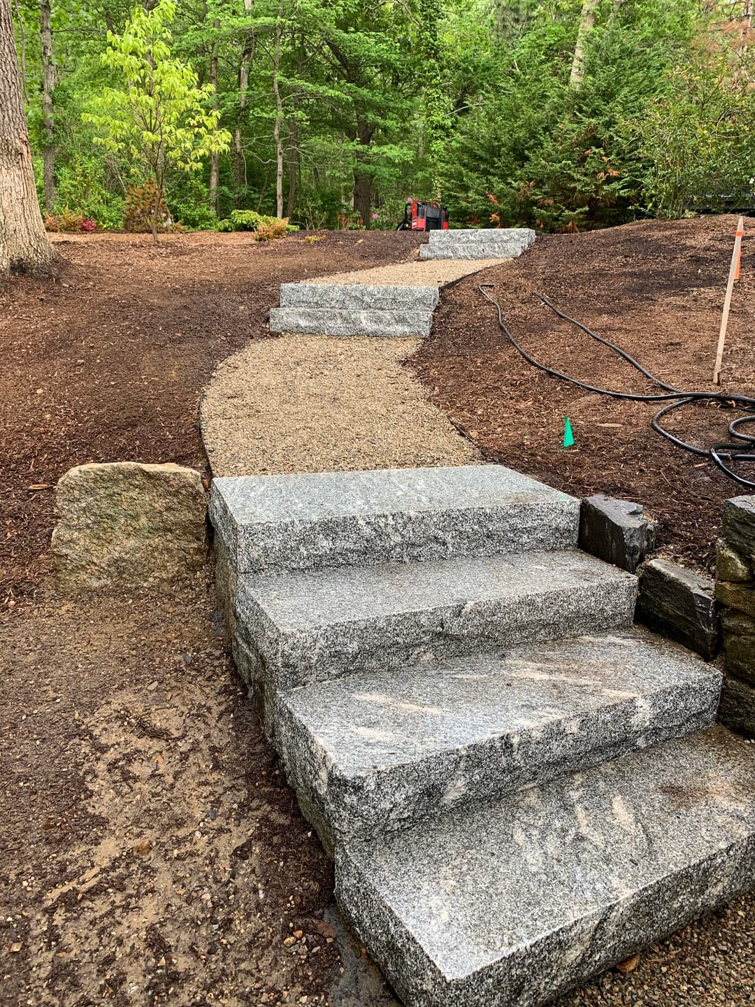 Granite stone steps lead up a gravel path in a lush, green garden setting.