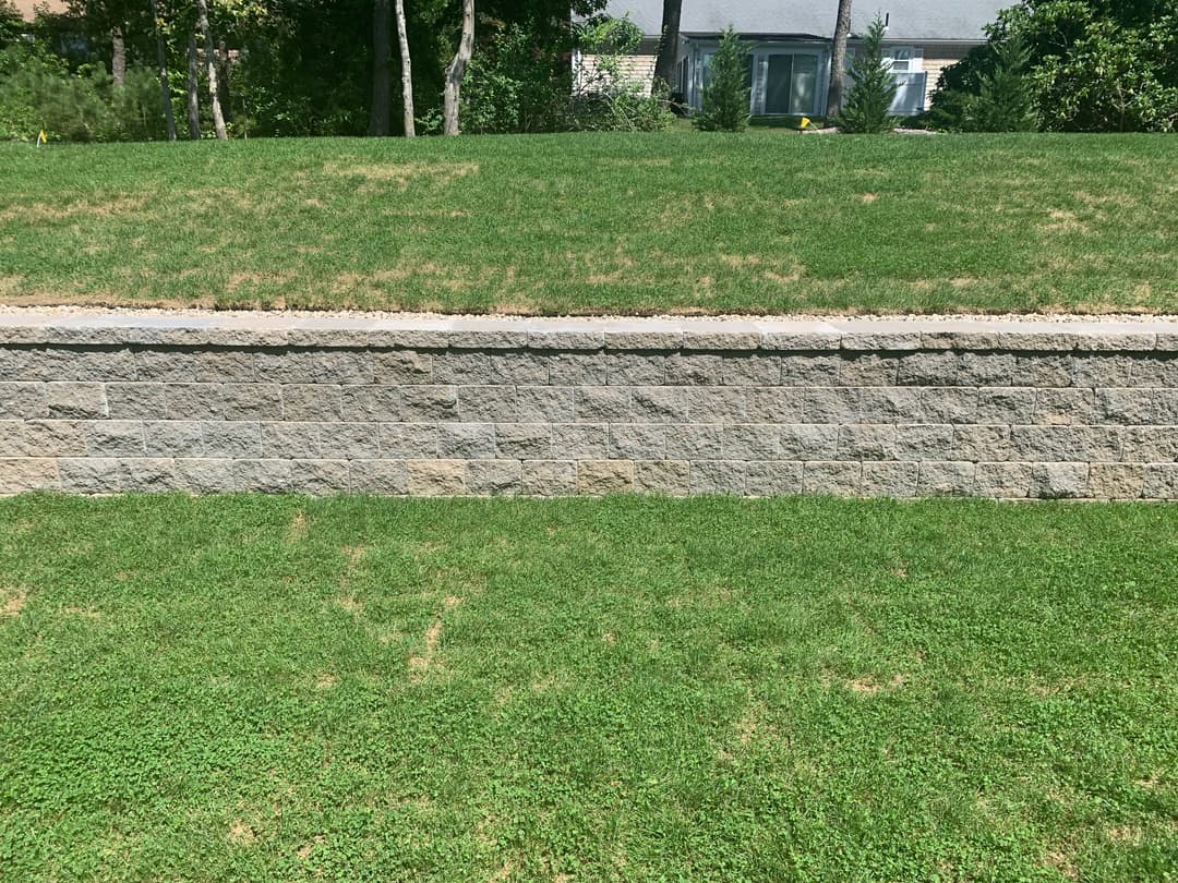Landscape with a stone retaining wall and lush green grass under a clear sky.