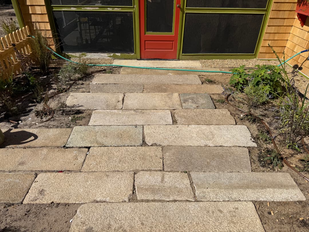 Stone pathway leading to a red door, surrounded by greenery and landscaping.