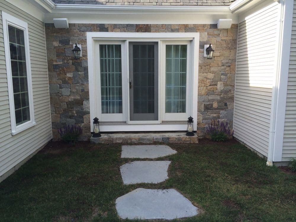 Stylish stone entryway with double doors, pathway, and lanterns in a residential setting.