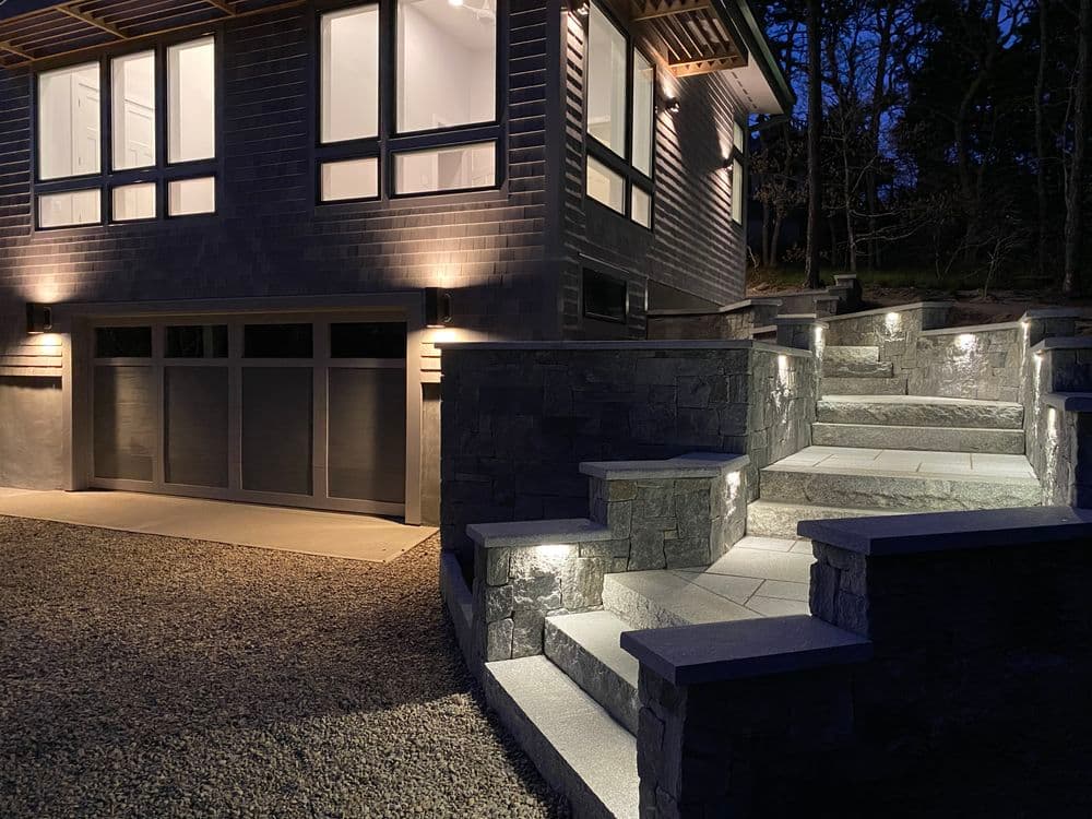 Modern home exterior with illuminated stone steps and driveway, featuring stylish lighting.