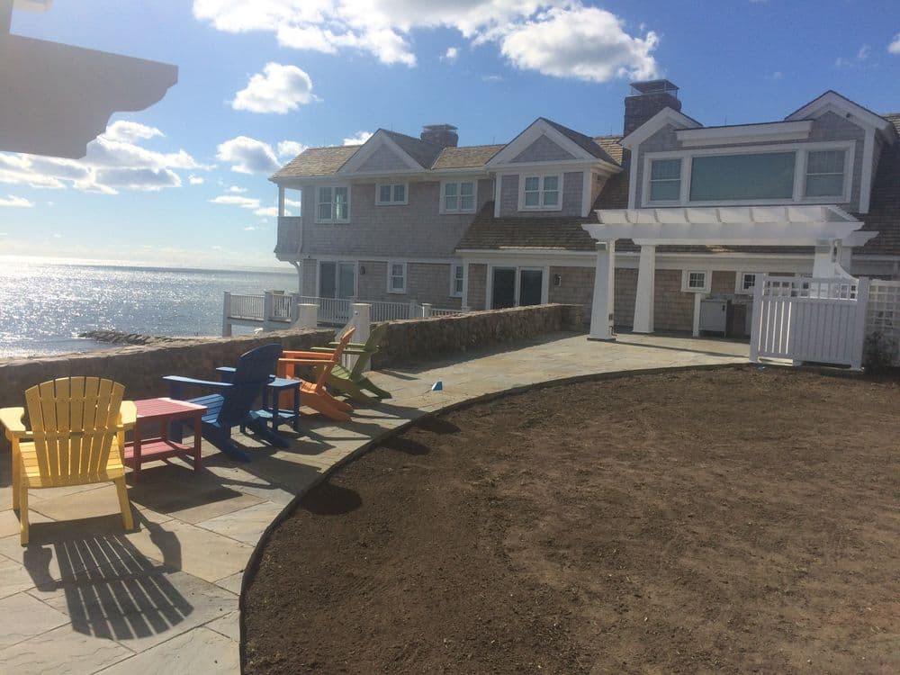 Coastal house with colorful Adirondack chairs overlooking the sea on a sunny day.