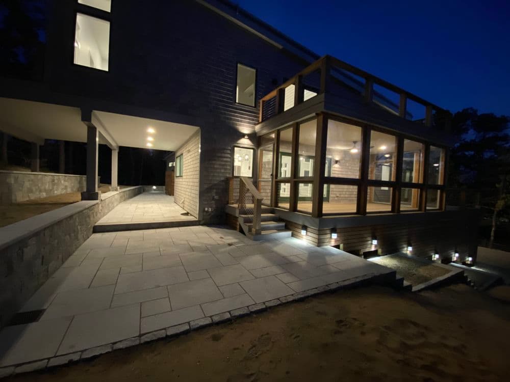 Modern home exterior at night with illuminated pathways and a glass-enclosed porch.