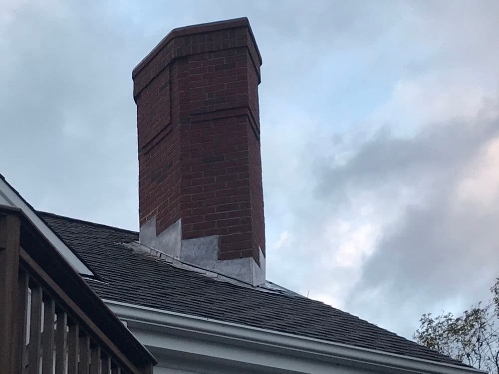 Brick chimney on a residential roof under a cloudy sky, showcasing roofing details.