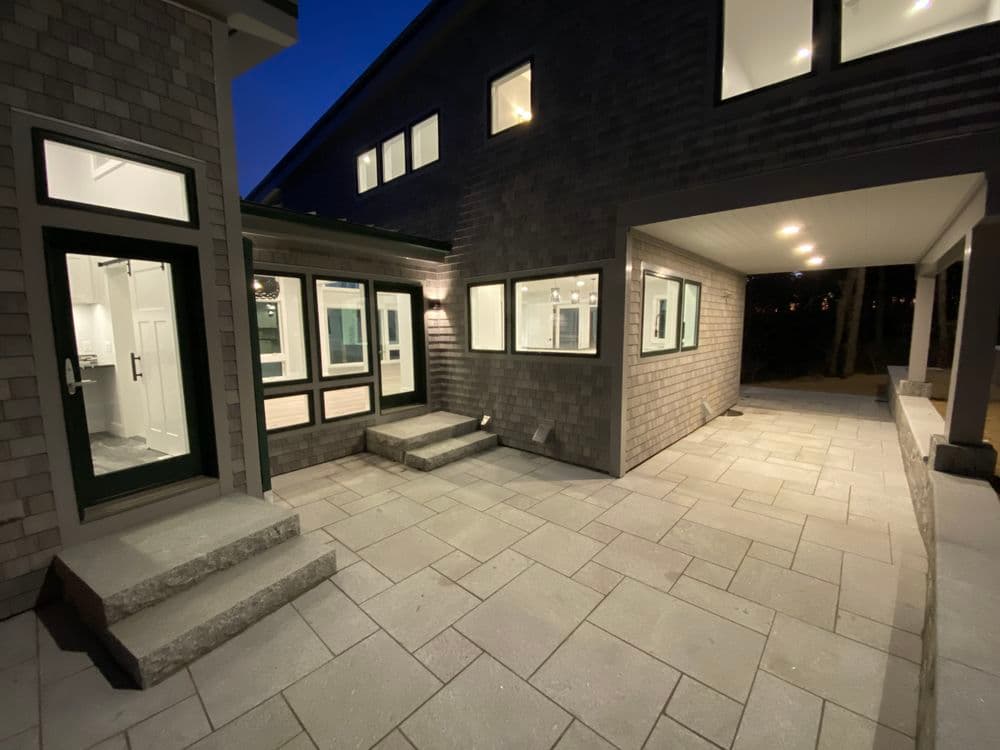 Modern home exterior with spacious patio and large windows, illuminated at night.