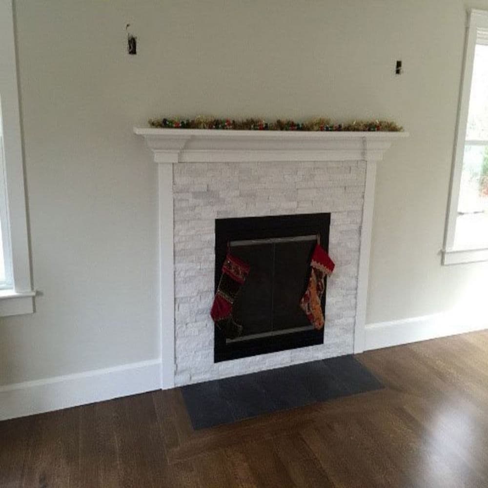 Modern white stone fireplace with stockings, neutral walls, and hardwood flooring.